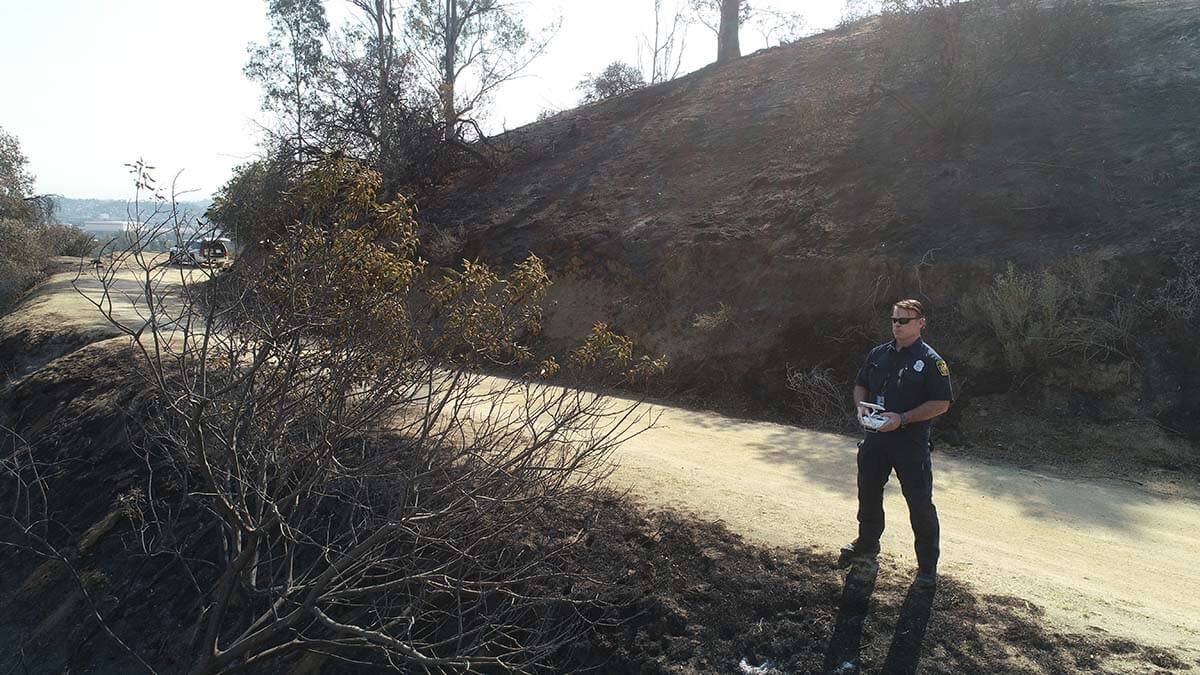 A man standing on a dirt road near a burned area.